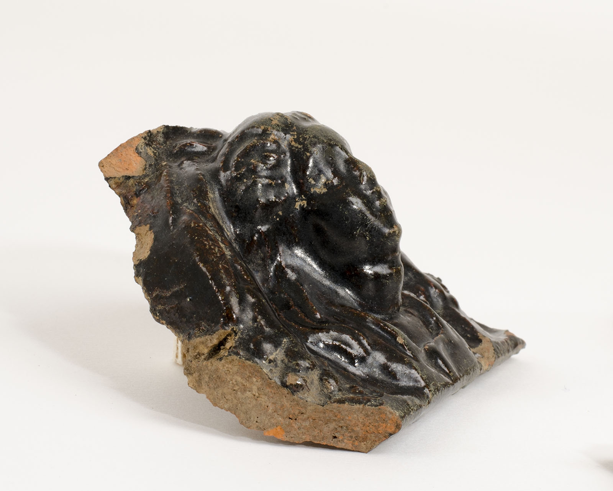 Reliefmönstrat med växtdekor samt människofigur, svartglaserat.