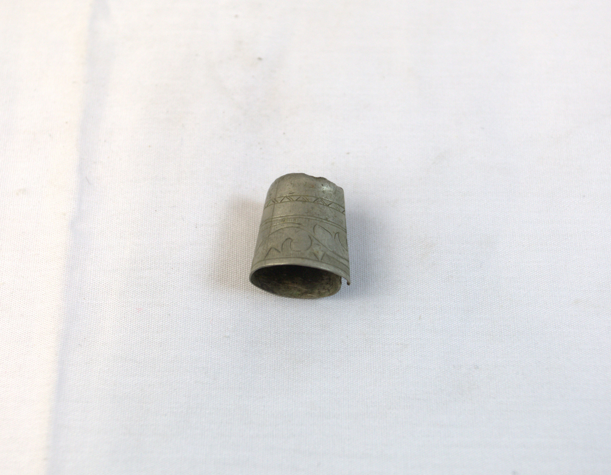 Gjenstand i tynt metall. Metallet har mønser og bøyd i en sirkelform.