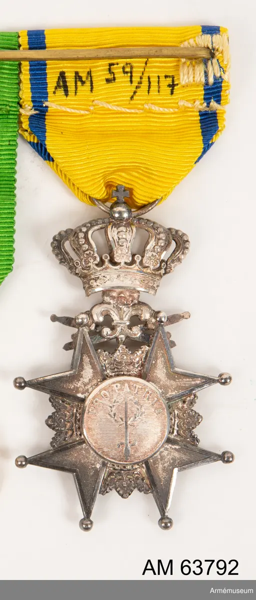 Grupp M II.
Svärdsmannatecken med band tilldelat styckjunkaren Georg Wilhelm Wessman.  Ett snedställt johannitkors av silver. Åtta uddar, var och en slutande i en kula. Mellan korsarmarna öppna kronor. På åtsidan har tecknet en blå, emaljerad glob i korstets mitt med ett stolpvis ställt svärd och tre öppna kronor ställda två och en. Mellan korsets övre vänstra udd och övre högra störtande svärd. Frånsidans mittglob är av silver med ett stolpvis ställt svärd omlagt med två kvistar ovanför "PRO PATRIA". Tecknet hänger i en kunglig krona. Medaljband av ett 35 mm brett sidenripsband - gult med mörkblå kantrand. 