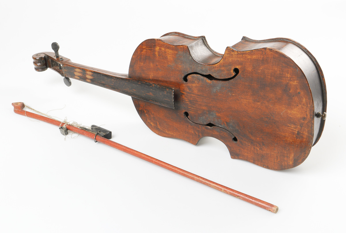 Fiol av allmogetillverkning, helt gjord av trä. Fiolen har två svartmålade stämskruvar. Ljudhålen på locket är f-formade. Strängfäste, stall, strängar och två stämskruvar saknas. Tillhörande stråke.