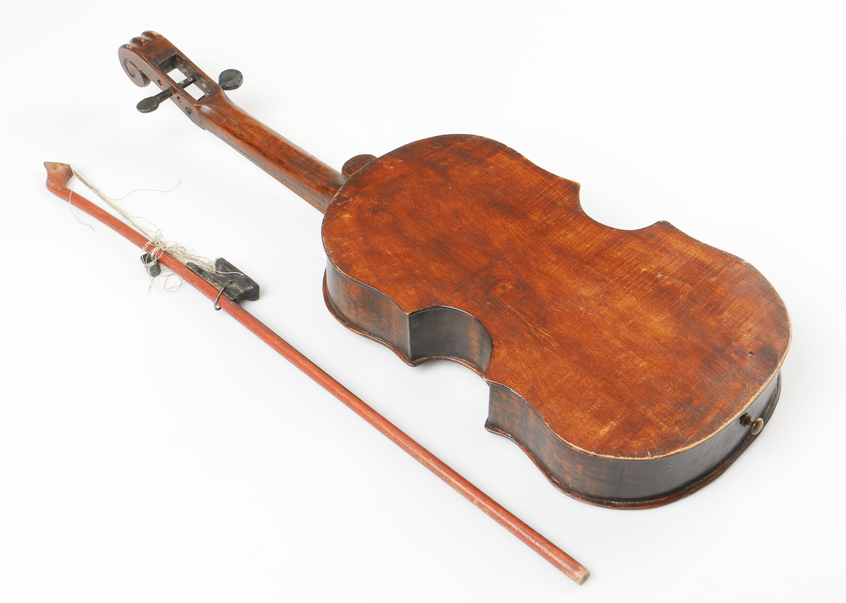 Fiol av allmogetillverkning, helt gjord av trä. Fiolen har två svartmålade stämskruvar. Ljudhålen på locket är f-formade. Strängfäste, stall, strängar och två stämskruvar saknas. Tillhörande stråke.