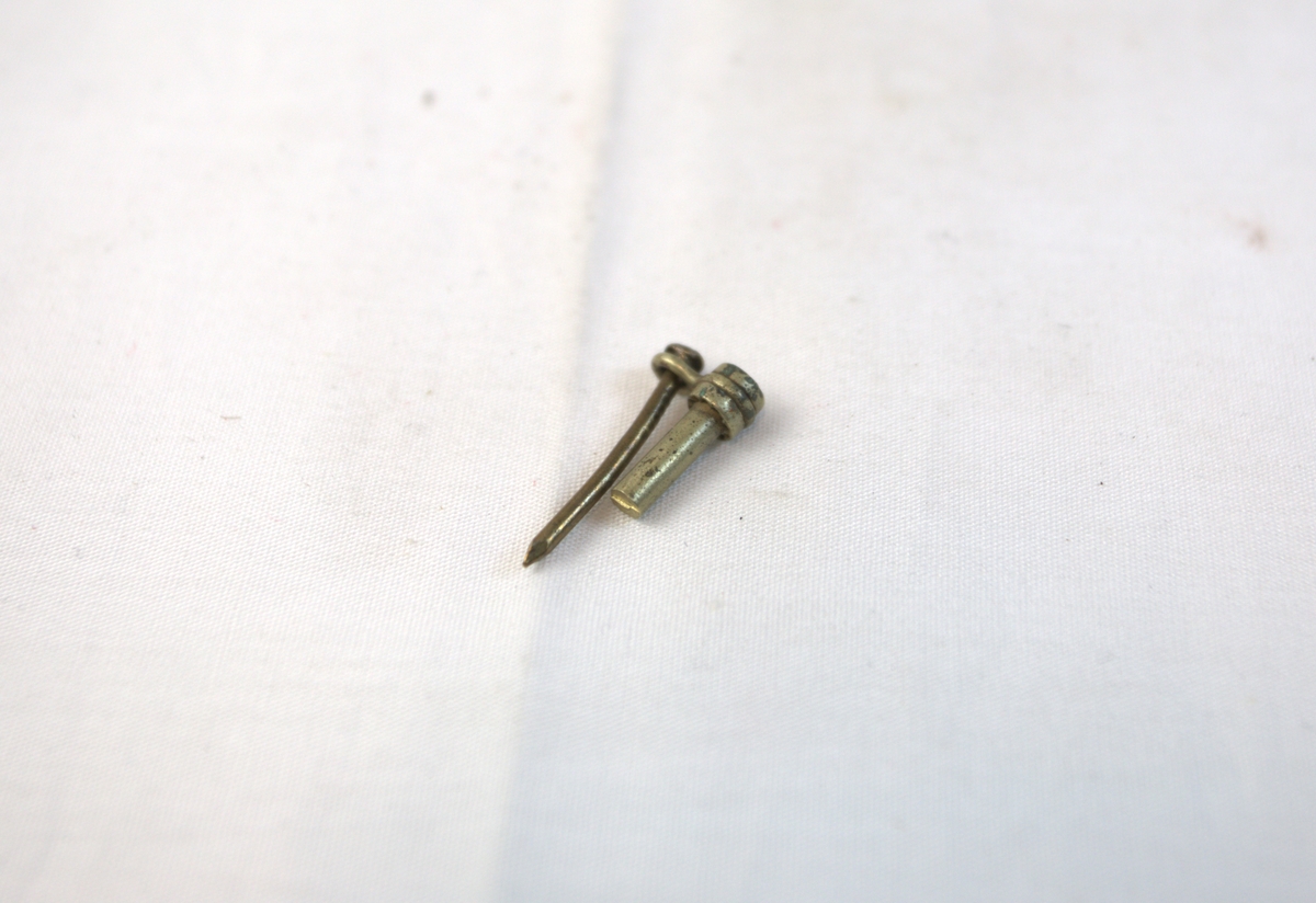 Gjenstand i messing. Gjenstanden består av en spiker som sitter i en ring festet i den andre delen. 