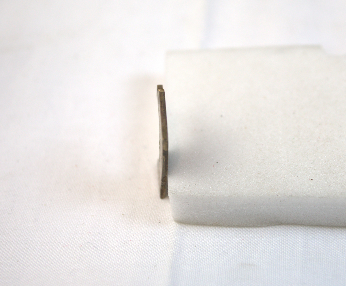 Flat metallgjenstand med spor etter skjæring. 