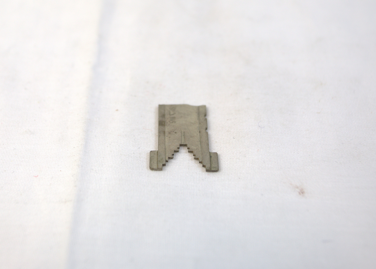 Flat metallgjenstand med V-formet ende på den ene siden. I V-formen er det hakk.