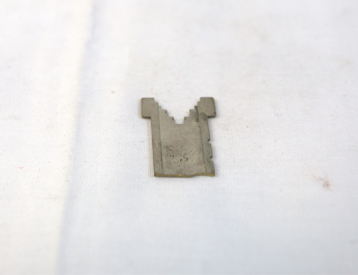 Flat metallgjenstand med V-formet ende på den ene siden. I V-formen er det hakk.