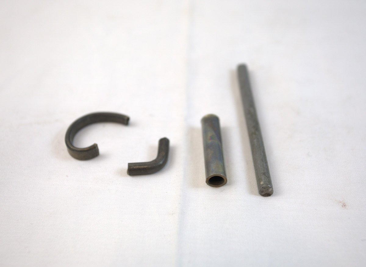 Fire metallgjenstander. To av dem er bøyd, en er avlang og rett, mens en er rørformet.