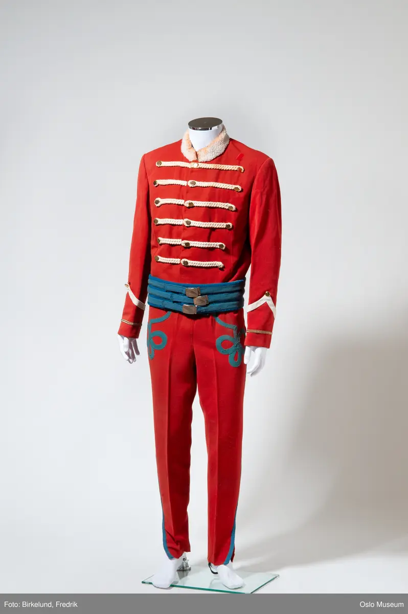 A: bukse, røde med applikasjon
B: jakke: rød med hvite snorer og brunt "skinnfor"
C: jakke, rød med hvite snorer og blått belte