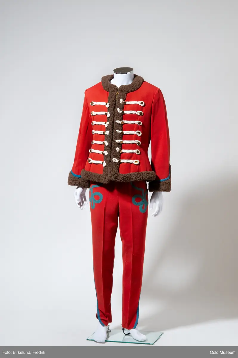 A: bukse, røde med applikasjon
B: jakke: rød med hvite snorer og brunt "skinnfor"
C: jakke, rød med hvite snorer og blått belte