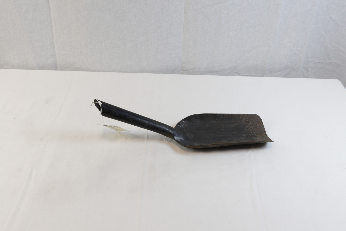 Spade til bøtte til å bære koks i. Spaden er noe rusten og har et hull på enden av håndtaket. 