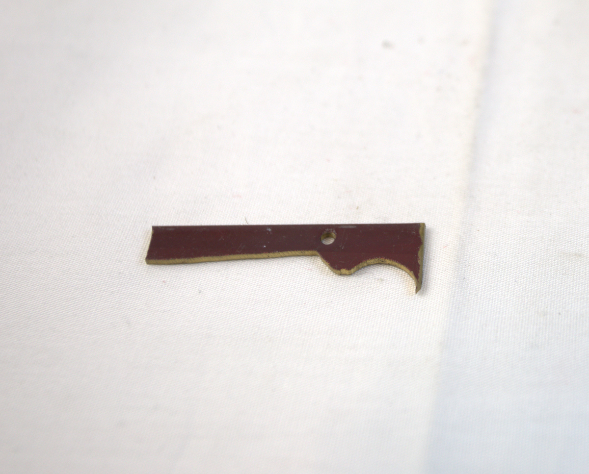 Metallgjenstand i rød- og gullfarge. Trolig brukt som materiale i gullsmedvirksomhet.