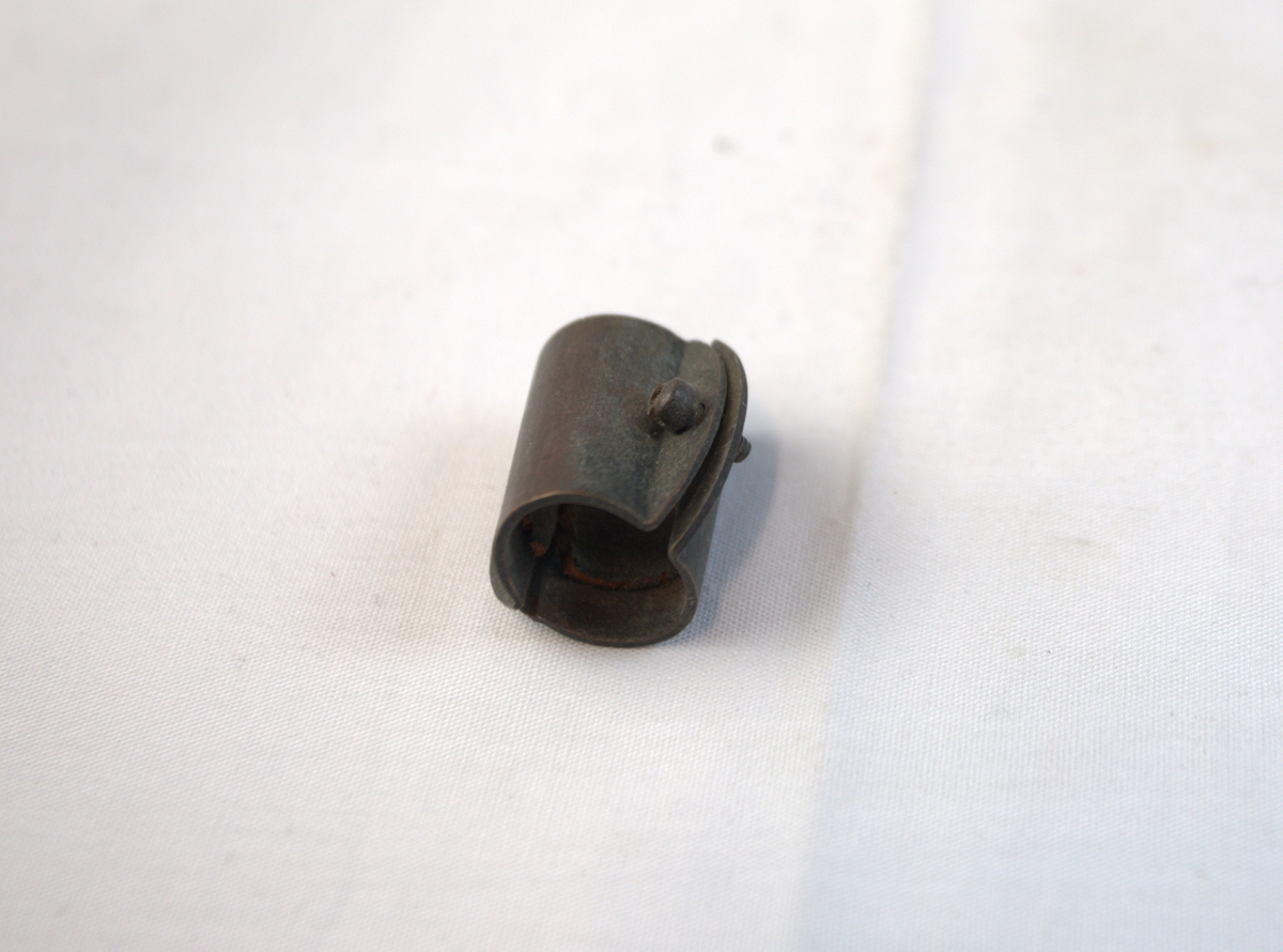 Metallgjenstand i to deler, festet sammen av to skruer. Gjenstanden er buet slik at den former en sirkel.