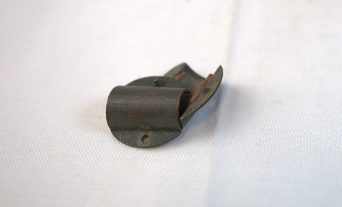 Metallgjenstand i to deler, festet sammen av to skruer. Gjenstanden er buet slik at den former en sirkel.