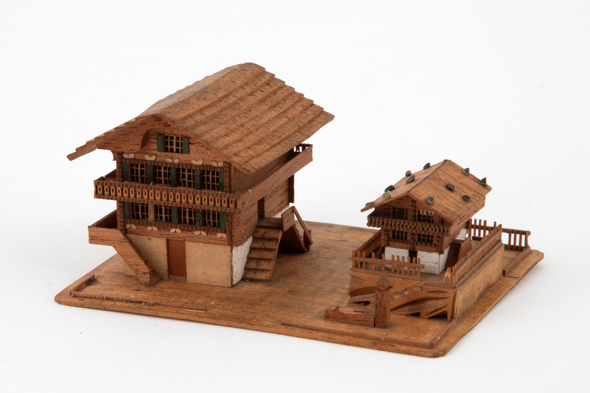 Husgruppe i miniatyr på en rektangulær plate: to sveitserhus, et stort og et mindre, med altaner og store sadeltak. Fint utskårne detaljer i vinduer og rekkverk.