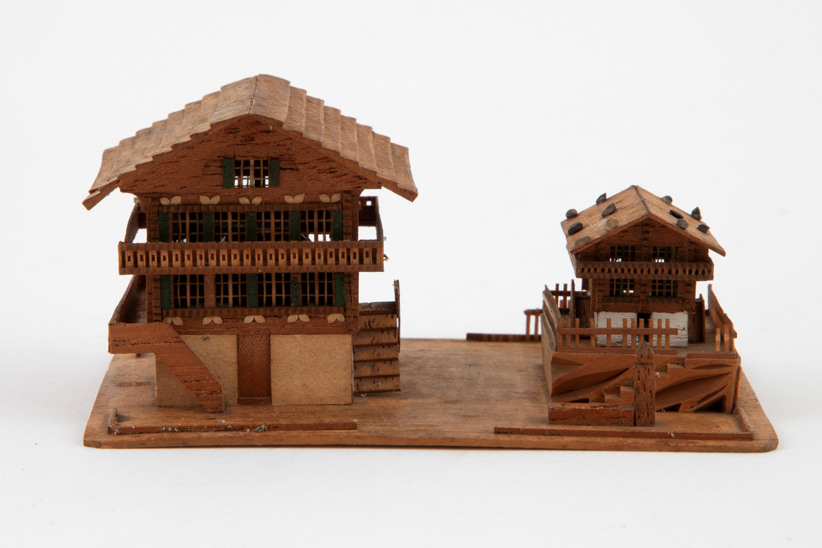 Husgruppe i miniatyr på en rektangulær plate: to sveitserhus, et stort og et mindre, med altaner og store sadeltak. Fint utskårne detaljer i vinduer og rekkverk.
