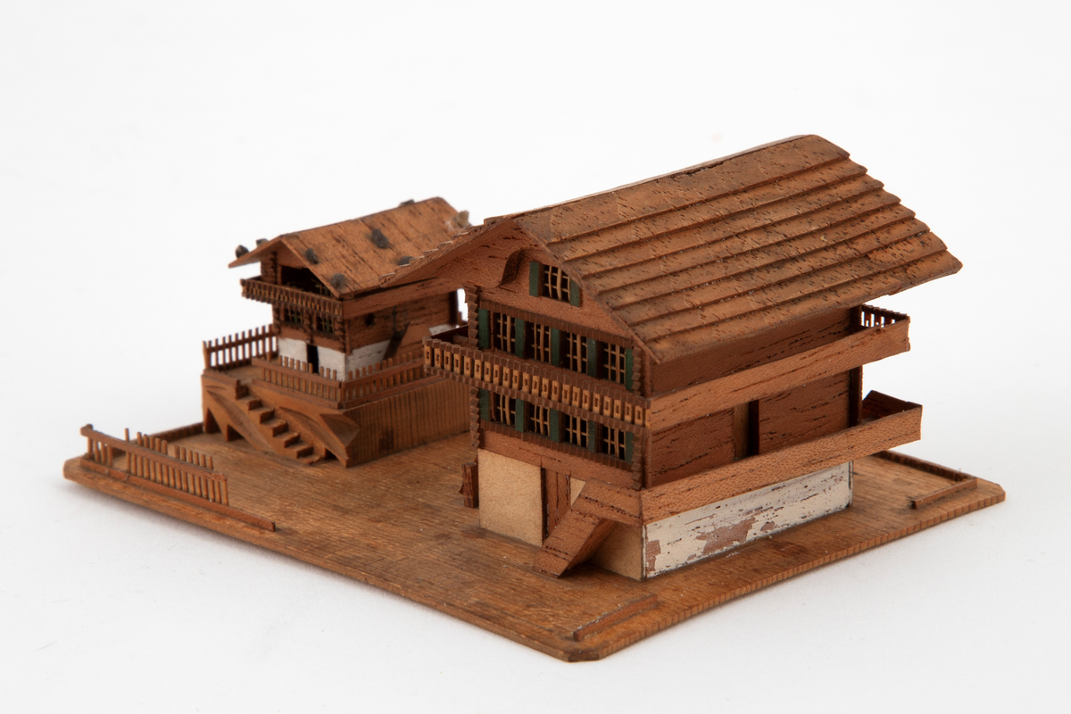 Husgruppe i miniatyr på en rektangulær plate: to sveitserhus, et stort og et mindre, med altaner og store sadeltak. Fint utskårne detaljer i vinduer og rekkverk.