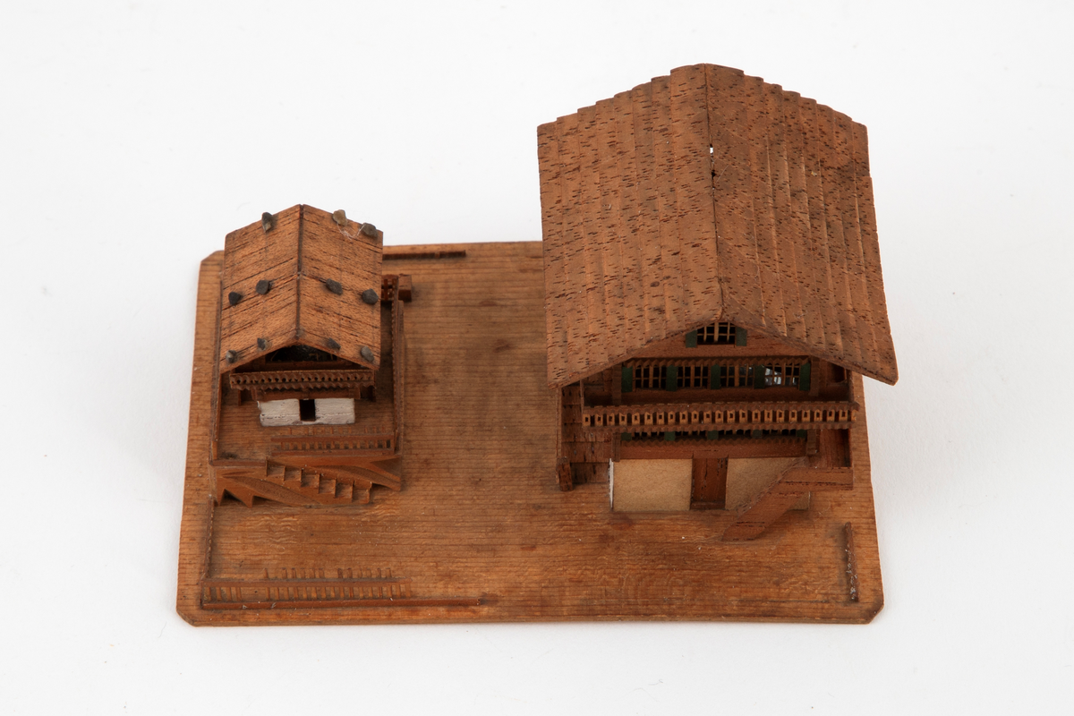 Husgruppe i miniatyr på en rektangulær plate: to sveitserhus, et stort og et mindre, med altaner og store sadeltak. Fint utskårne detaljer i vinduer og rekkverk.