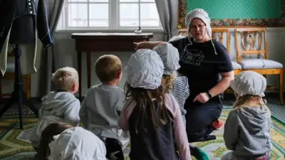 En gruppe med barn sitter på gulvet og hører på omviseren fortelle. 