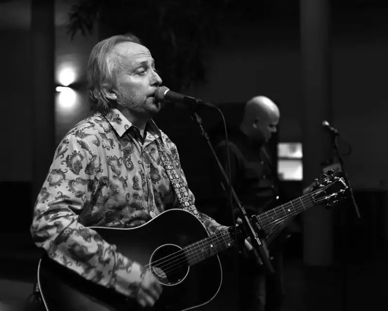 Svart/hvit bilde av Levi Henriksen som synger i mikrofon og spiller gitar. 