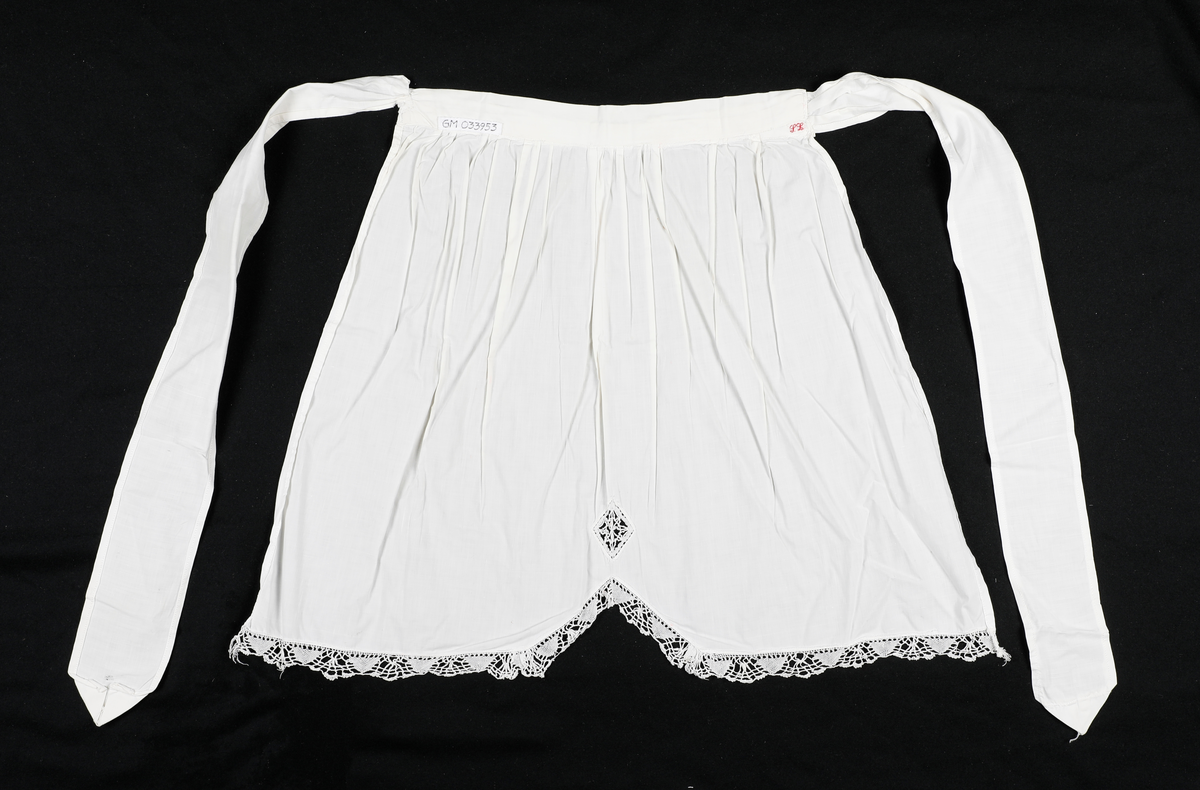 Forkle med påsydd blondekant nederst. Nedkanten på forkleet går opp i en spiss på midten.