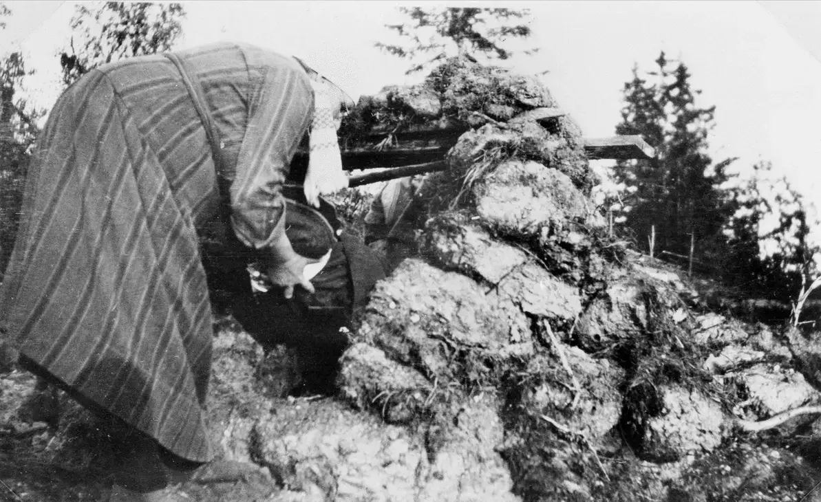 Gammal svartvit bild från omkring 1930, av en kvinna som jorddrar ett barn.