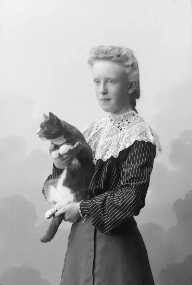 Flicka i klänning och spetskrage håller en katt i famnen. Svartvit bild, omkring sekelskifte 1900.