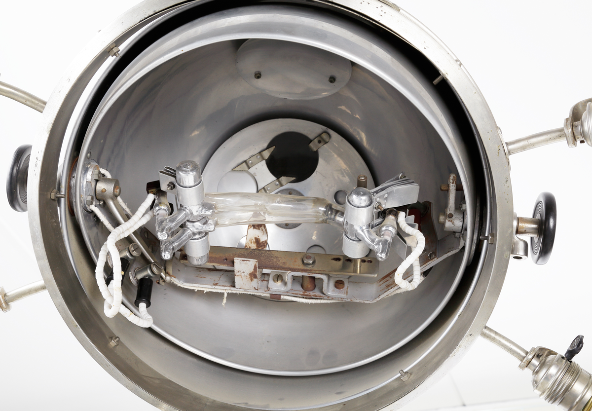 Kvartslampa som består av en förnicklad pelare med en höj- och sänkbar lampa. Lampan har ett klot vars innehåll  är en kvartslampa med kvicksilver som bildar UV-ljus. Huven har en öppningsbar del som kan öppnas med en låsbar ratt på ena sidan så själva lamphuset kan kommas åt. Denna öppningsbara del har en vridbar skiva med hål i olika storlek, 15-ca. 45mm, detta så att man kan ha olika koncentration på ljusstrålen. På andra sidan finns en motsvarande ratt som man kan justera själva kvartslampan. Runt om klotet sitter åtta stycken skärmförsedda lamphållare där varannan lamphållaren har en vridströmbrytare så att varanna lampa kan släckas. Dessa lamphållare har lampfästen i vitt porslin, och vridströmbrytarna är troligen i bakelit. Det sitter även två stycken elkontakter i porslin på klotets utsida. Foten på lampan består av en cirkelformad svartlackerad välvd platta med tre stycken vridbara dubbelhjul. På huvens utsidan sitter även två tillverkarskyltar fastnitade som har texten "QUARZLAMPEN-GESELLSCHAFT m.b.H. HANAU No. 38673, 7,8/3,8 Amp. 110/220 Volt." och "KÜNSTLICHE HÖHENSONNE QUARZLAMPEN-GESELLSCHAFT HANAU".