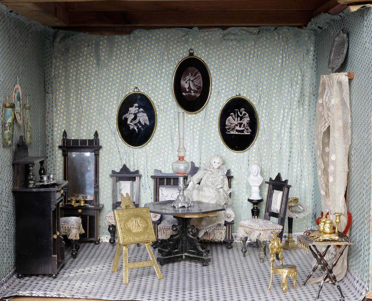 Dockskåp med tillhörande inredning. Brunbetsat träskåp försett med glasförsedda pardörrar. Skåpet har tre våningsplan med fem möblerade rum. Inredning från 1890-talet. Skåpet står på fyra svarvade fötter.