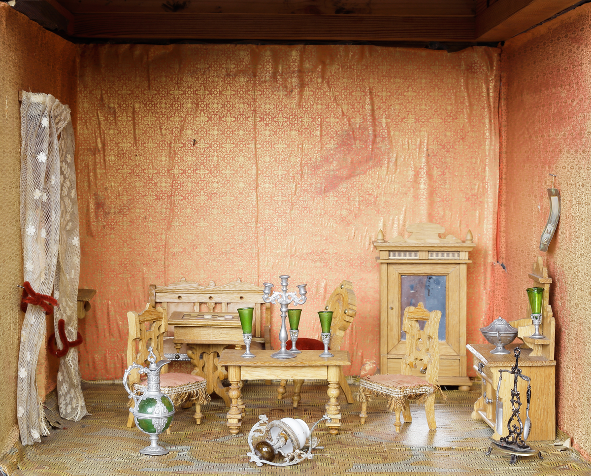 Dockskåp med tillhörande inredning. Brunbetsat träskåp försett med glasförsedda pardörrar. Skåpet har tre våningsplan med fem möblerade rum. Inredning från 1890-talet. Skåpet står på fyra svarvade fötter.