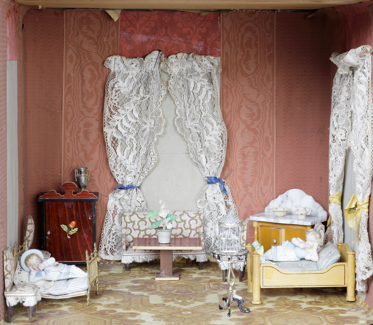 Dockskåp med tillhörande inredning. Brunbetsat träskåp försett med glasförsedda pardörrar. Skåpet har tre våningsplan med fem möblerade rum. Inredning från 1890-talet. Skåpet står på fyra svarvade fötter.