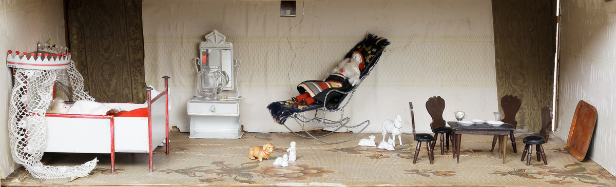 Dockskåp med tillhörande inredning. Brunbetsat träskåp försett med glasförsedda pardörrar. Skåpet har tre våningsplan med fem möblerade rum. Inredning från 1890-talet. Skåpet står på fyra svarvade fötter.