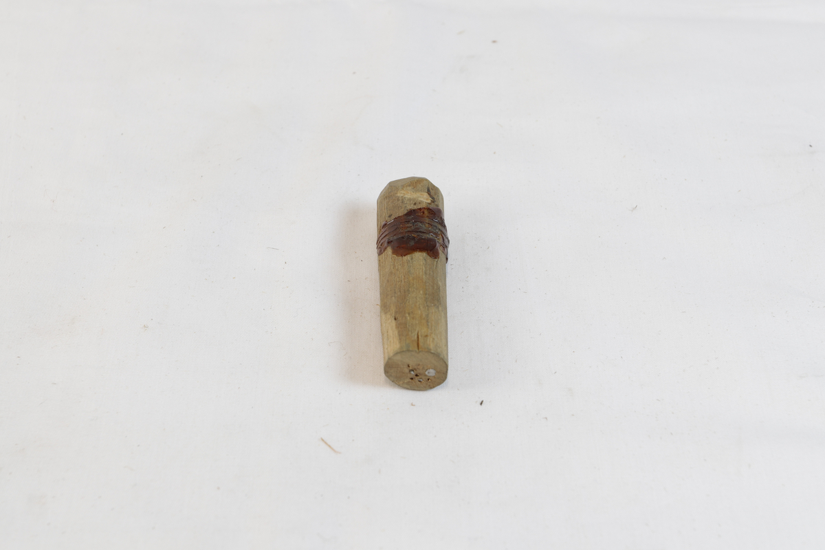 Tregjenstand med noe materiale på. Gjenstanden har spikere i seg.