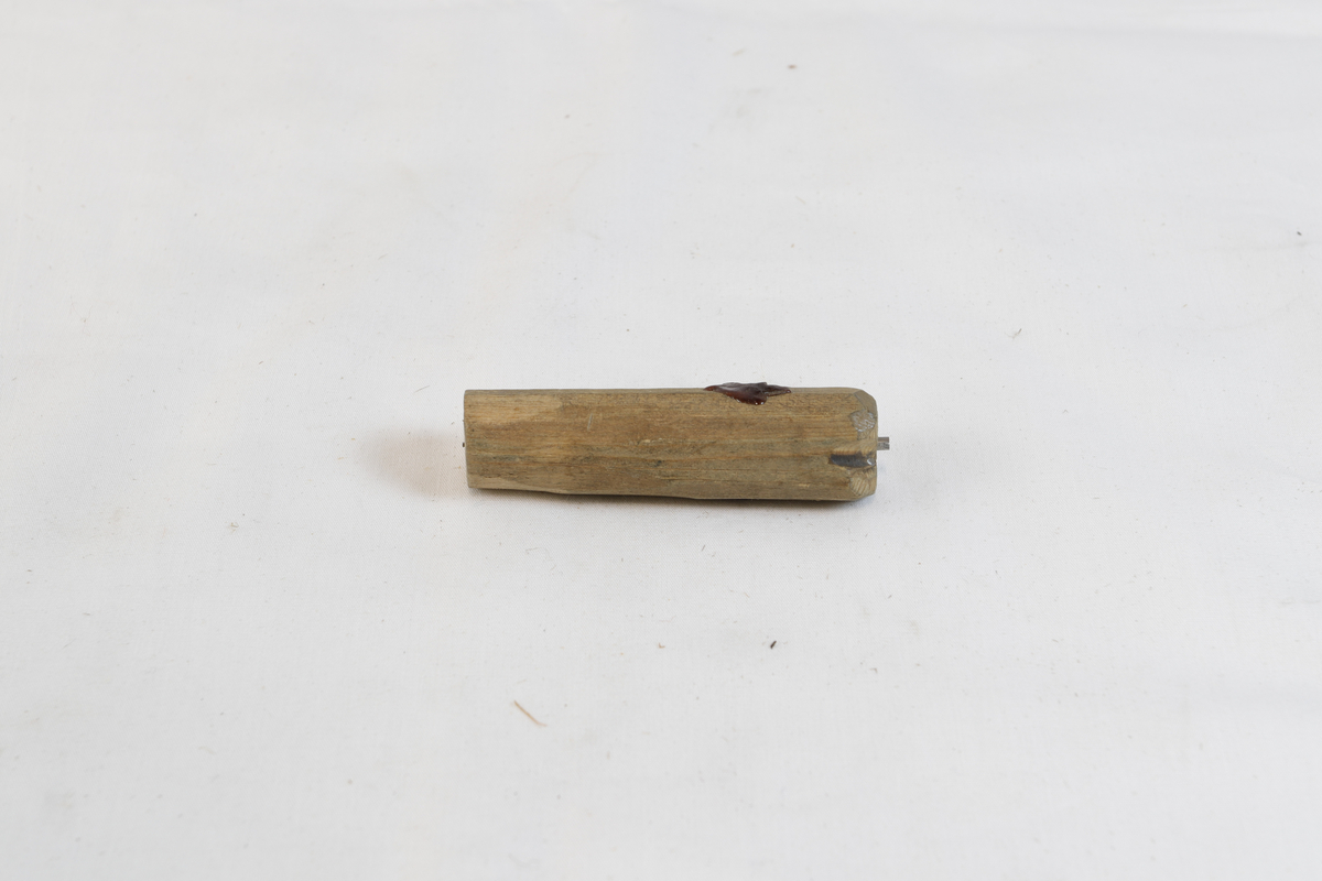 Tregjenstand med noe materiale på. Gjenstanden har spikere i seg.