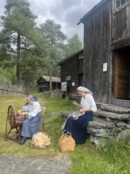 To jenter som sitjar utanfor eit gamalt hus og spinnar