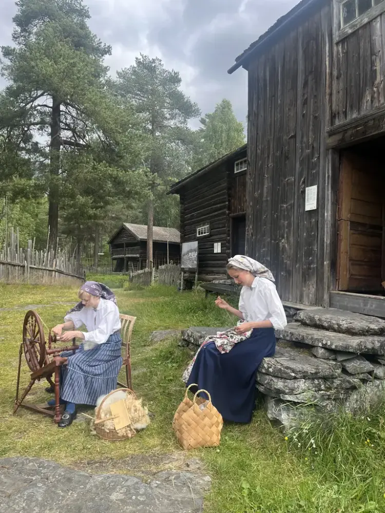 To jenter som sitjar utanfor eit gamalt hus og spinnar