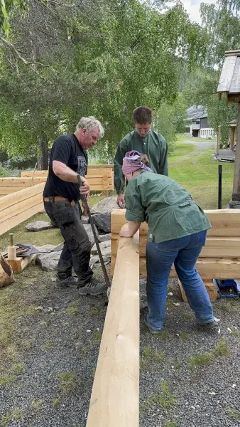 Instruktør som viser to elevar korleis ein setjer saman laftade stokkar
