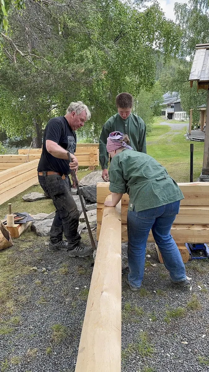 Instruktør som viser to elevar korleis ein setjer saman laftade stokkar