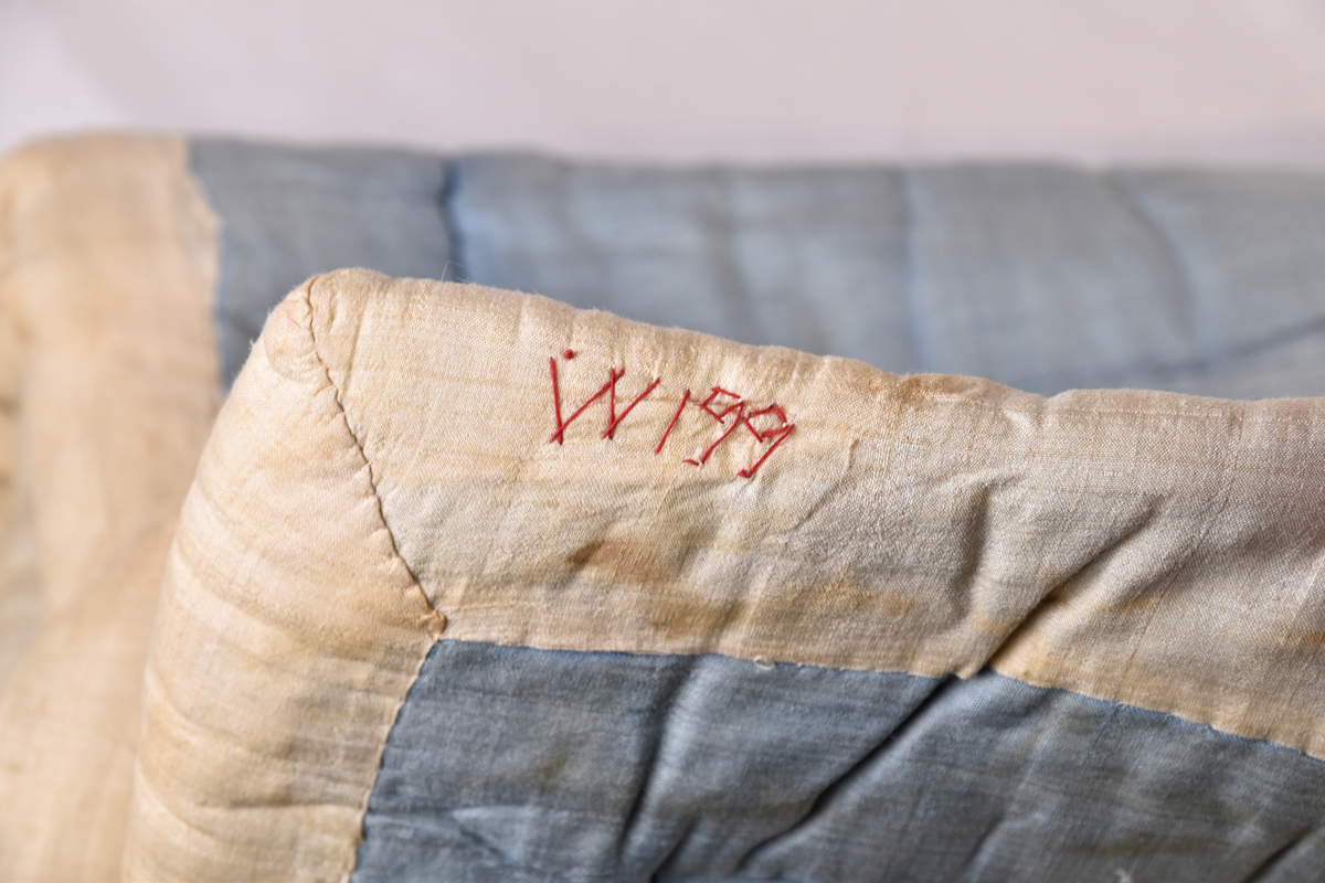 Teppe til Svithun barnevogn. Det er hvitt med blomstertrykk over og blått under. Brodert med rød tråd: "W199" eller "WI99" eller "WISS".