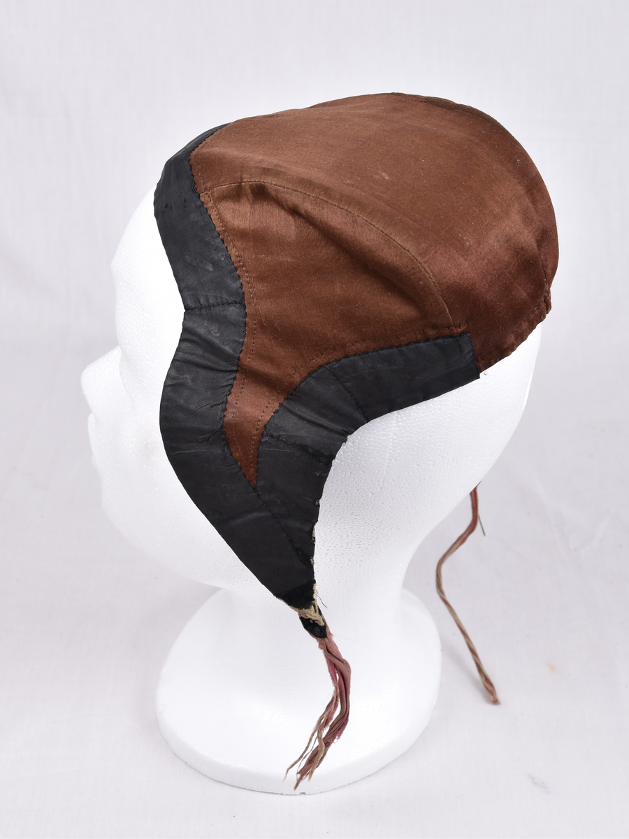 Damelue med gyllenbrunt silkstoff og svart kant. Foret er stripete.