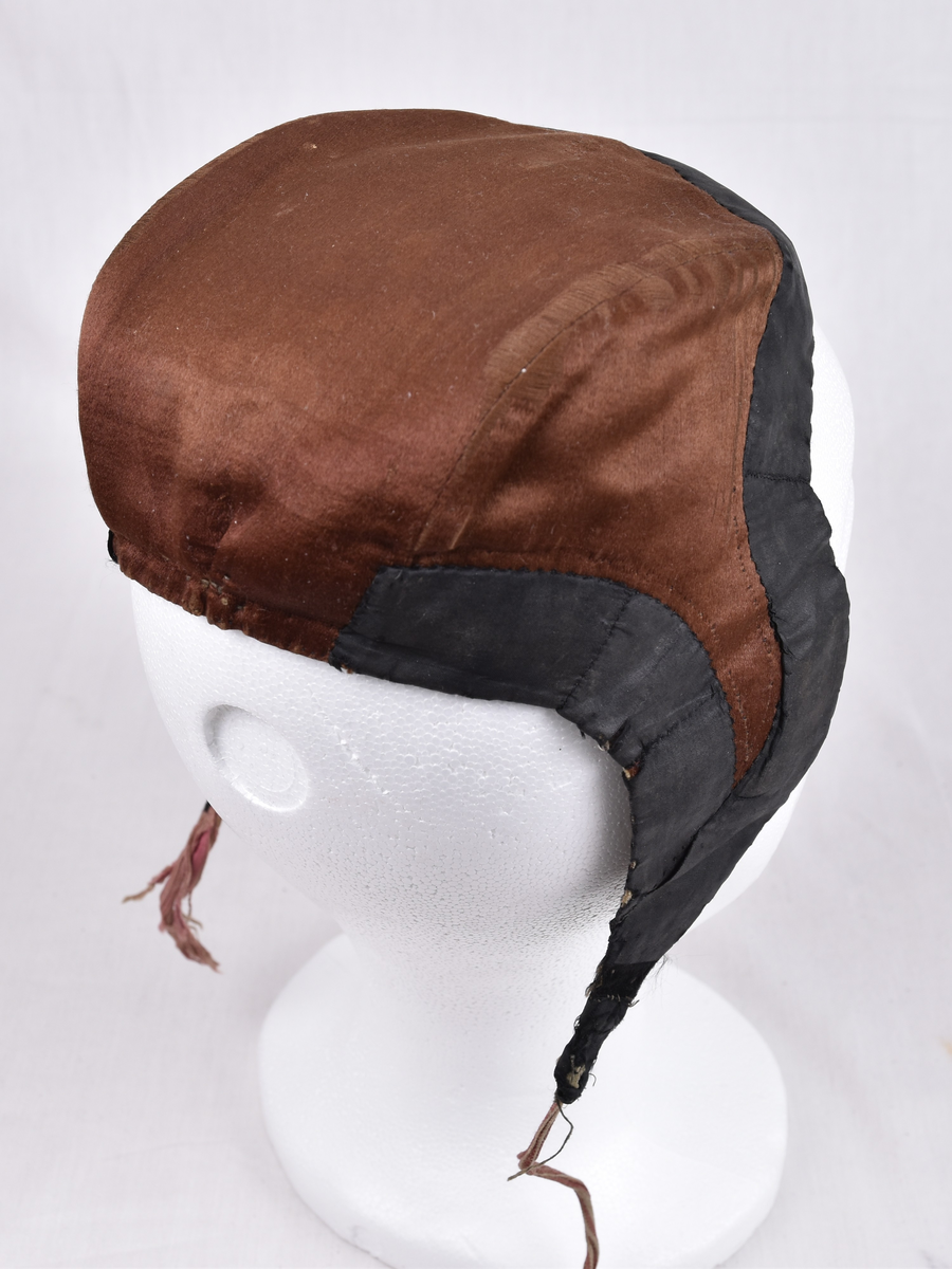 Damelue med gyllenbrunt silkstoff og svart kant. Foret er stripete.