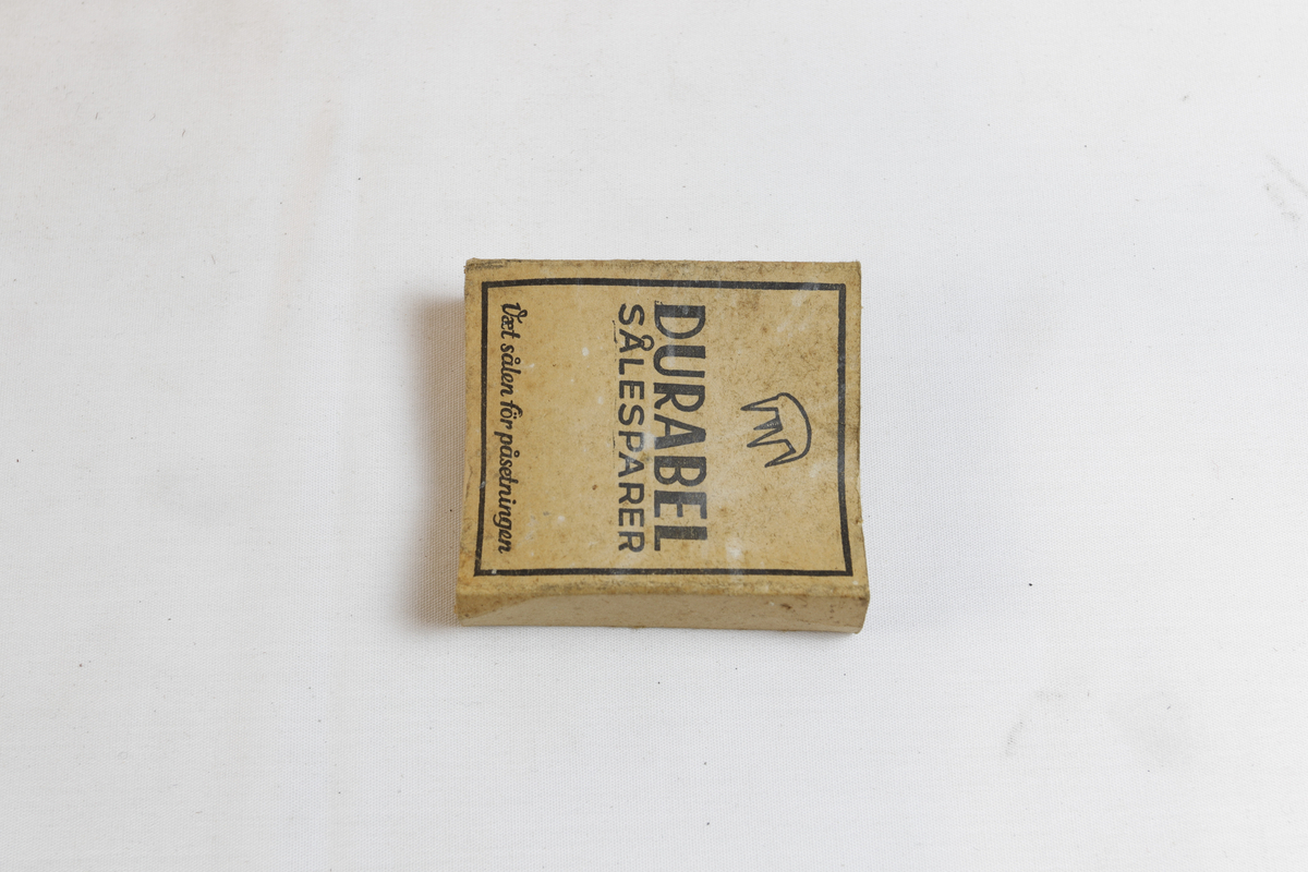 Rektangulær eske som inneholder sirkulære sålesparer med tre pigger.
