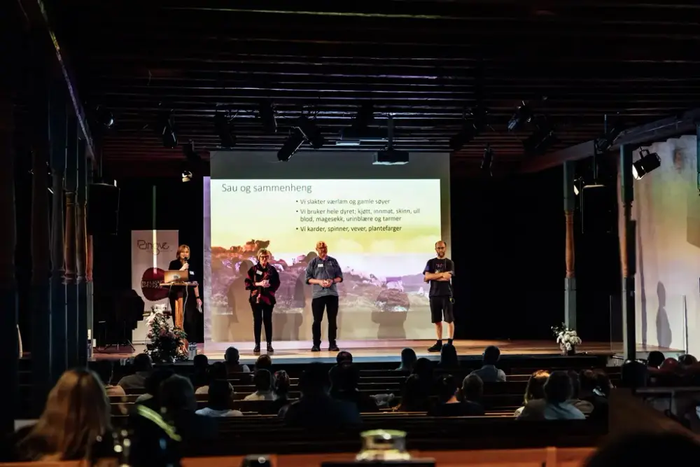 Fire mennesker som står på en scene med publikum foran