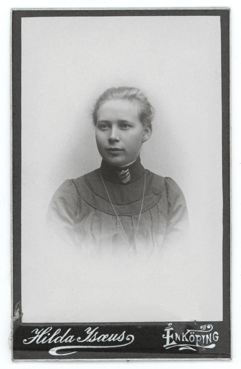 Svartvit porträtt av okänd dam med möjligt frälsningsarméns emblem på halsen.