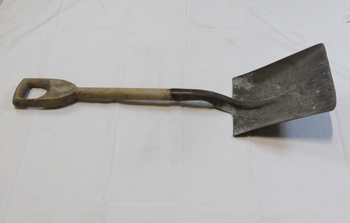 Spade med trehåndtak. 
Treverket har hull fra borebiller eller liknende.
En innskrift på håndtaket er visket bort og uleselig. 