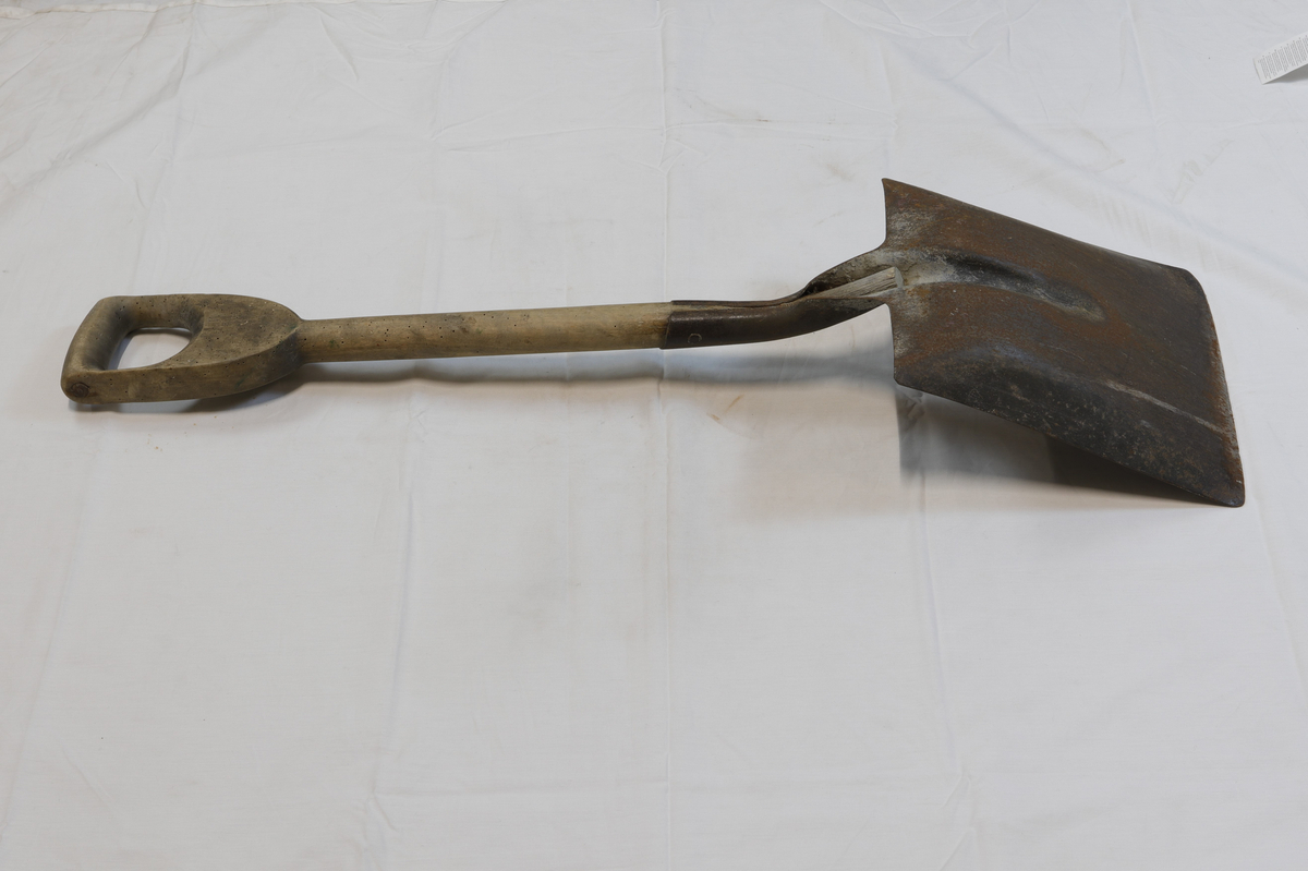 Spade med trehåndtak. 
Treverket har hull fra borebiller eller liknende.
En innskrift på håndtaket er visket bort og uleselig. 