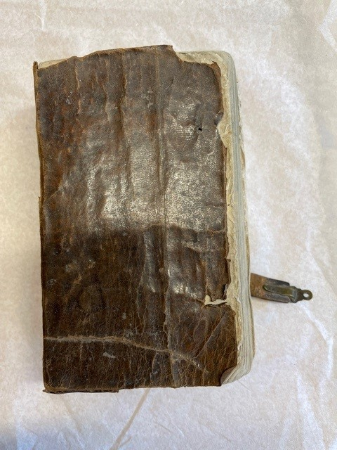 Psalmbok, tryckt i Stockholm, helfranskt band, pärm skadad men ursprungligen klädd med papper. Försättsblad med titel 
"Den Swenska Psalm-Boken. af Konungen Gillad och Stadfästad, år 1819. STOCKHOLM, tryckt i R. Ecksteins Tryckeri, 1820. Skomakare-Embetets Hus, hörnet af Slottsbacken och Bollhusgränden".  Försättsblad dekorerad med tryck föreställande postamen, och villande lyra samt rökformation. På baksidan del av spänne av läder med fäste i mässing

