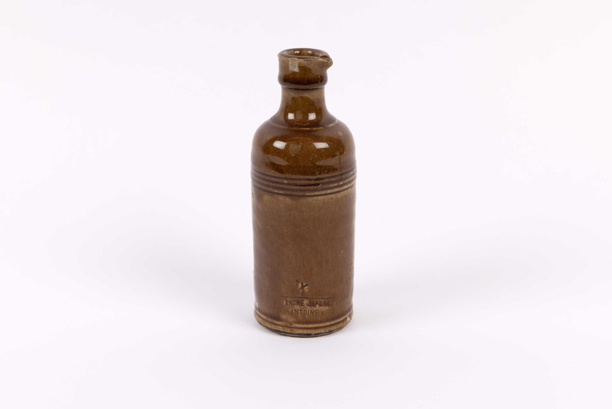 Keramikkrukke funnet ved Tollboden i Bergen. Liten, sylinderformet krukke med smal hals og helletut. Dreid krukke med riller mot hals i glassert keramikk. Trolig fra rundt 1870 årene.