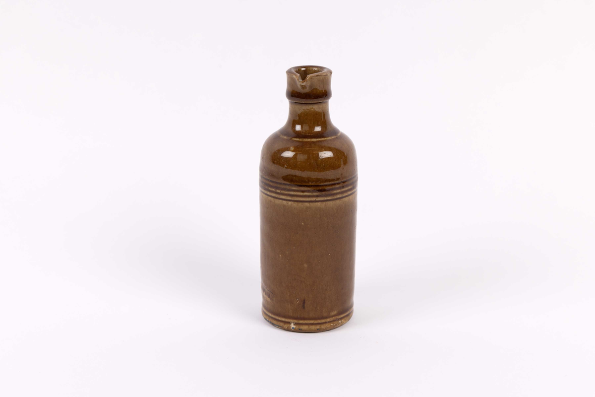 Keramikkrukke funnet ved Tollboden i Bergen. Liten, sylinderformet krukke med smal hals og helletut. Dreid krukke med riller mot hals i glassert keramikk. Trolig fra rundt 1870 årene.