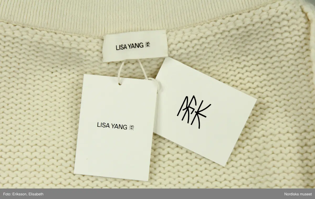 Kjol, stickad av vitt kashmirgarn. Kort modell. Upptill resårstickad linning, strax därunder smal, stickad, horisontal remsa, vikt uppåt. Nedtill dekorstickning.  
På insidan av linningen (bak) vit tygetikett med text: LISA YANG". Vid denna etikett fäst med vitt snöre två pappersetiketter.
Fastknutet med vitt snöre i etiketten bak två pappersetiketter. Den ena med text "LISA YANG. Den andra med kinesiskt tecken (använt som firmans symbol) samt text: 
"Style. Lovi / Colour: Cream / Size: 1 / Style no.: 2023326".
Vid linningen också fäst tre vita tygetiketter med information om tillverkning, material, tvätt mm. samt liten etikett med storleksangivelse (1).
/Leif Wallin 2025-03-05