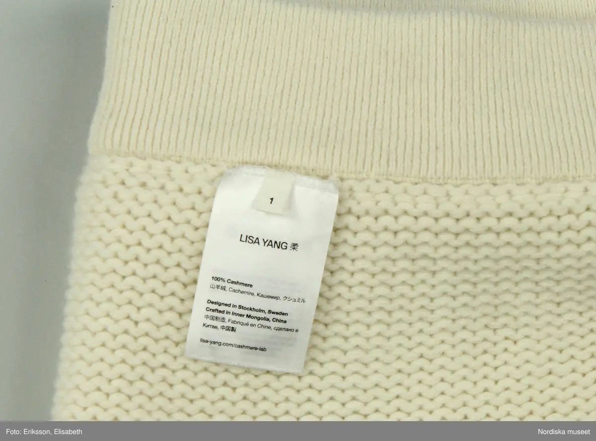 Kjol, stickad av vitt kashmirgarn. Kort modell. Upptill resårstickad linning, strax därunder smal, stickad, horisontal remsa, vikt uppåt. Nedtill dekorstickning.  
På insidan av linningen (bak) vit tygetikett med text: LISA YANG". Vid denna etikett fäst med vitt snöre två pappersetiketter.
Fastknutet med vitt snöre i etiketten bak två pappersetiketter. Den ena med text "LISA YANG. Den andra med kinesiskt tecken (använt som firmans symbol) samt text: 
"Style. Lovi / Colour: Cream / Size: 1 / Style no.: 2023326".
Vid linningen också fäst tre vita tygetiketter med information om tillverkning, material, tvätt mm. samt liten etikett med storleksangivelse (1).
/Leif Wallin 2025-03-05