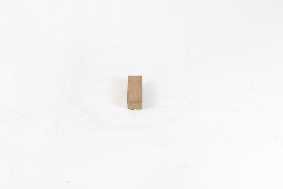 Stempel i tre. Stempelet har en rektangulær form med motiv av en litenbokstav. Bokstav: å. Det er svart trykksverte på stempelet.